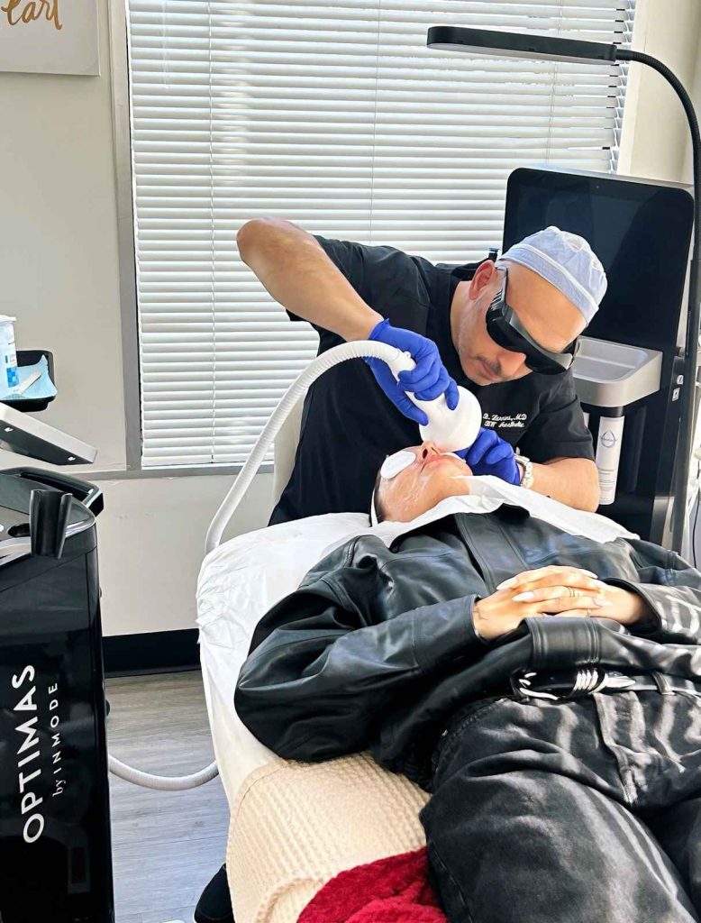 Physician performing a Lumecca IPL facial treatment using an INMODE Optimus machine on a patient wearing a leather jacket, emphasizing the clinical setting.