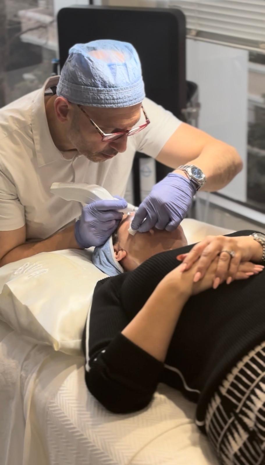Dr. Zarrini, an aesthetic specialist in Beverly Hills, performing a precision laser skin rejuvenation treatment on a patient's facial area using a professional handheld laser device in a clinical medical spa setting.